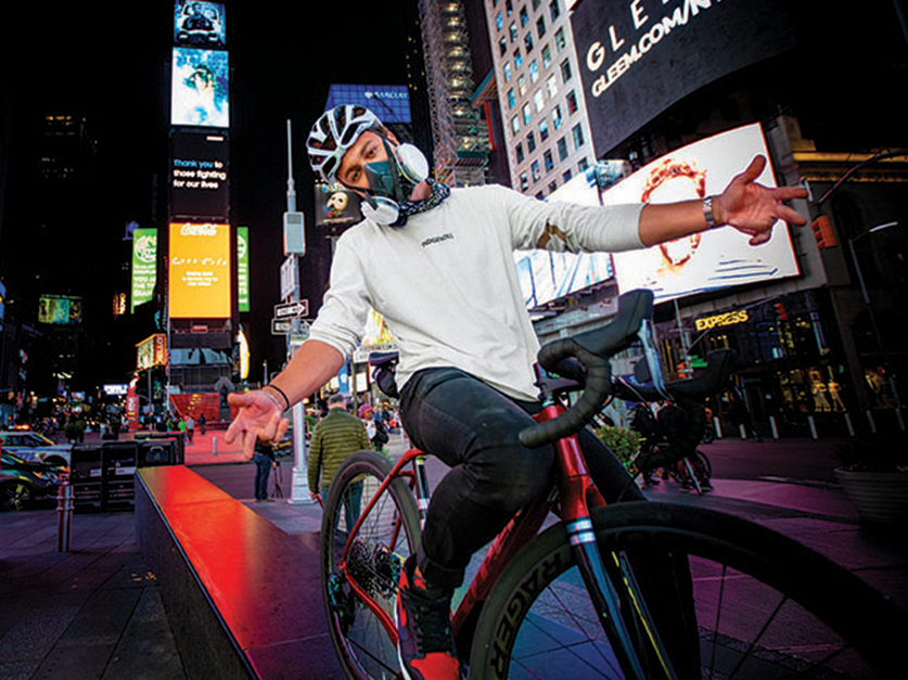 Close up of Julien Howard a.k.a. Velo Barber riding bicycle with New York's Time Square in the background