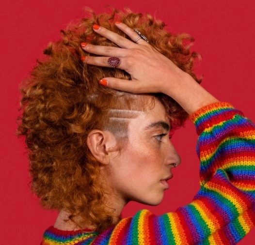 Small image of girl with red hair, rainbow sweater on red background